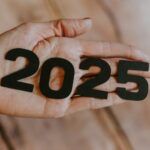 A person's hand holding the number twenty twenty five.