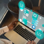 A person using a laptop with digital UI and UX interface graphics projected above the screen, illustrating concepts of user interface and user experience design.