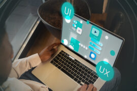 A person using a laptop with digital UI and UX interface graphics projected above the screen, illustrating concepts of user interface and user experience design.