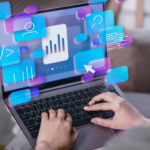 A person using a laptop with illustrated digital icons, including graphs, user avatars, and code, floating above the screen, symbolizing data analysis and technology.