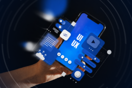 Hand holding a smartphone displaying blue UI and UX interface elements, surrounded by floating digital design components on a dark background.