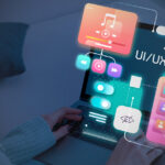 Person using a laptop with colorful digital UI/UX interface elements, such as music, video, settings, and user profiles, displayed over the screen, representing digital design and user experience concepts.